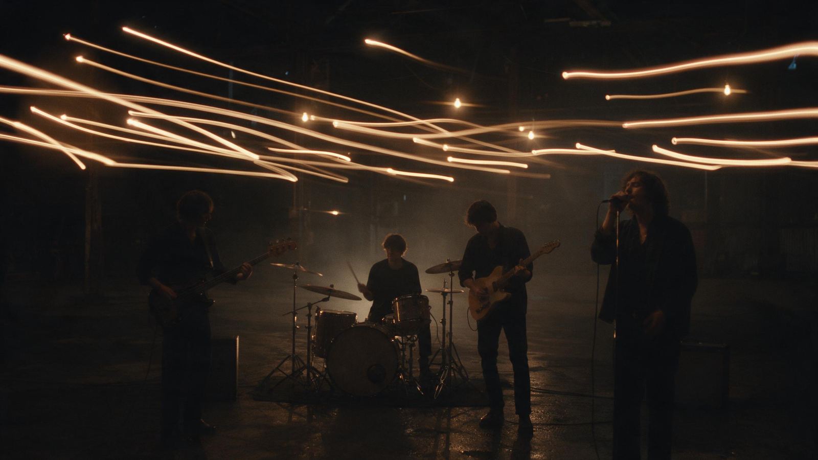 Music video still: a band performing in a warehouse with streaking light